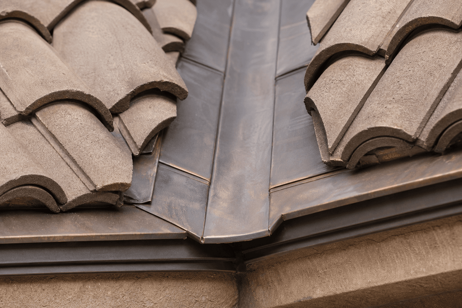 A rebuilt copper valley flashing running between courses of profile-matched terra-cotta clay tile.